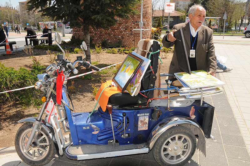 Eskişehir’de yaşayan 83 yaşındaki Ahmet Er, ilkokulda kum üzerine çizerek başladığı resim sanatını 70 yıldır sürdürüyor ve eserlerini motosikleti ile köy köy dolaşarak sergiliyor. 
